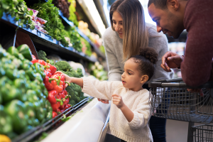 Young family shopping for vegetables with their cute daughter